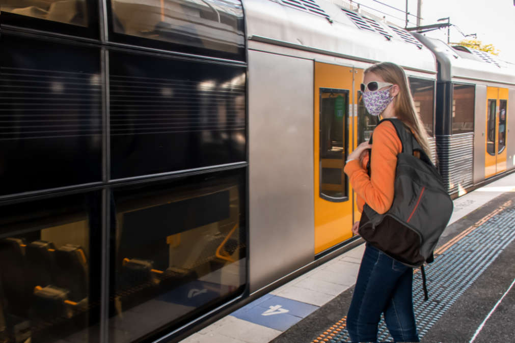 Teenage student girl wearing face mask waiting for the train on the station platform. 